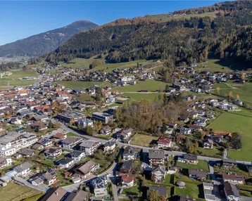 Weitläufige Luftaufnahme eines Dorfes in den Bergen mit vielen Wohnhäusern und grüner Landschaft.