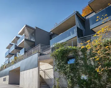 Moderne Architektur des Neubaus mit gestuften Balkonen, Glasbrüstungen und begrünten Fassadenelementen.