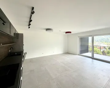 Heller offener Wohnbereich mit integrierter Küche, Fliesenboden und Zugang zum Balkon mit Bergblick.
