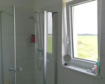Helles Badezimmer mit Duschkabine und Fenster, bietet Blick ins Grüne.