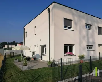Modernes Einfamilienhaus mit kleinem Garten, Terrasse und Sitzgelegenheiten im Freien an einem sonnigen Tag.