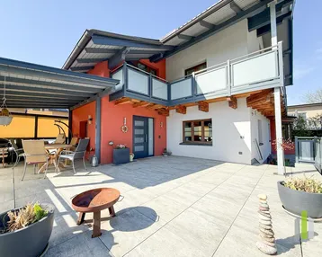 Große, sonnige Terrasse mit überdachtem Sitzbereich und modernem Balkon am Haus.