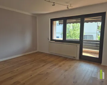 Helles Zimmer mit Holzboden und Zugang zu einem Balkon, ideal als Wohn- oder Schlafzimmer.