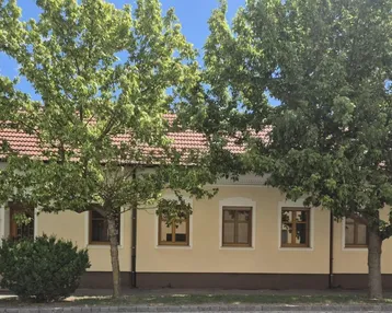 Traditionelles Einfamilienhaus mit heller Fassade und roten Ziegeln, umgeben von Bäumen.