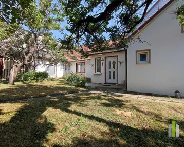 Weißes Einfamilienhaus mit rotem Ziegeldach und einem Vorgarten mit Bäumen und Rasenfläche.