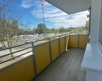 Geräumiger Balkon mit gelbem Geländer und Blick auf die Umgebung und eine belebte Straße.