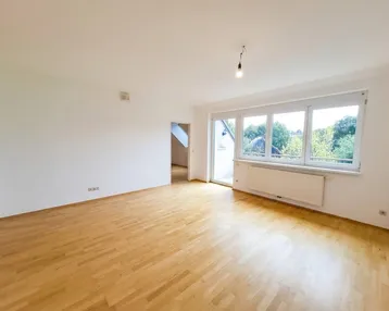 Helles Zimmer mit Parkettboden, weißen Wänden und Zugang zu einem Balkon.