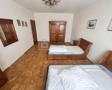Schlafzimmer mit zwei Betten, Holzschrank und Parkettboden in Fischgrätmuster.