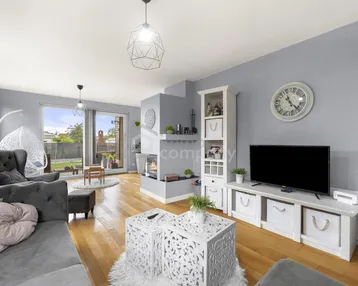 Helles Wohnzimmer mit modernem Kamin, Holzboden und großen Fenstern zum Garten.