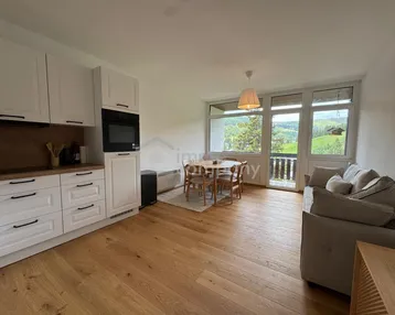 Helle Wohnküche mit Holzboden, weißen Schränken und Zugang zum Balkon mit Bergblick.