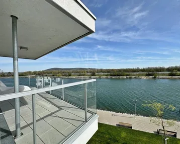 Geräumiger Balkon mit Fliesenboden und Glasgeländer, bietet einen weiten Blick auf den See.