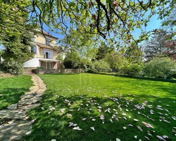 Großer, gepflegter Garten mit weitläufiger Rasenfläche, altem Baumbestand und einem Steinweg, der zum Haus führt.