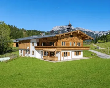 Traditionelles Holzhaus im alpenländischen Stil mit Bergblick und grüner Umgebung.