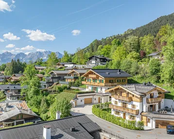 Panoramablick auf die alpine Villa und die umliegende Wohnsiedlung vor einer beeindruckenden Bergkulisse.