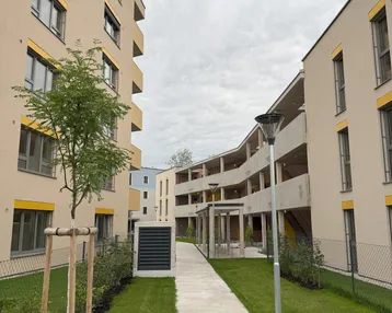 Neubaukomplex mit modernen Gebäuden, gepflegtem Rasen und Gehwegen unter bewölktem Himmel.