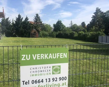 Verkaufsschild auf einem Zaun, der ein großes, grünes Grundstück mit Rasen und Bäumen zeigt.