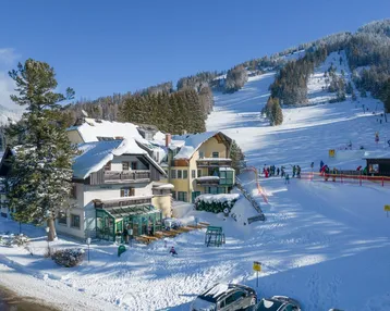 Hotelgebäude im Winter mit verschneiten Dächern und direktem Zugang zu den Skipisten.