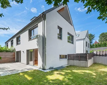 Modernes weißes Reihenhaus mit gepflegtem Garten und sonniger Terrasse unter blauem Himmel.