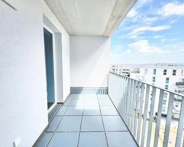 Heller Balkon mit Fliesenboden und Blick auf die umliegenden Gebäude und den Himmel.