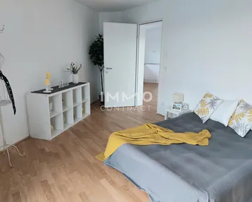 Helles Schlafzimmer mit Holzboden, modernem Bett und offener Tür zu einem weiteren Raum.