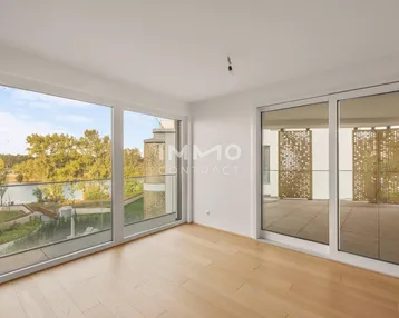 Helles Wohnzimmer mit Holzboden, großen Fenstern und Zugang zu einer Terrasse mit Seeblick.