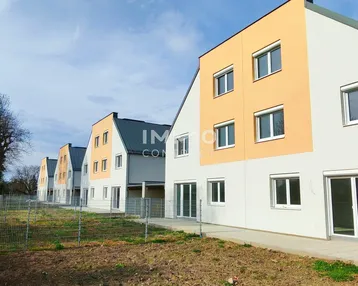 Reihe moderner Neubauten mit hellen Fassaden und großen Fenstern unter blauem Himmel.