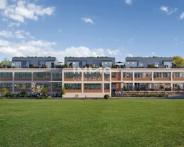 Moderne Wohnanlage mit großen Fenstern und Dachterrassen, umgeben von Grünflächen unter blauem Himmel.