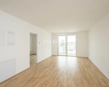 Lichtdurchfluteter Raum mit Holzparkett und Zugang zu einem französischen Balkon.