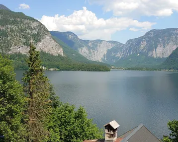 Panoramablick auf den See und die umliegenden Berge unter blauem Himmel.