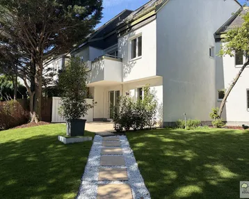 Gepflegter Gartenbereich mit Rasenfläche und Steinweg, der zum modernen Gebäude mit Terrasse führt.