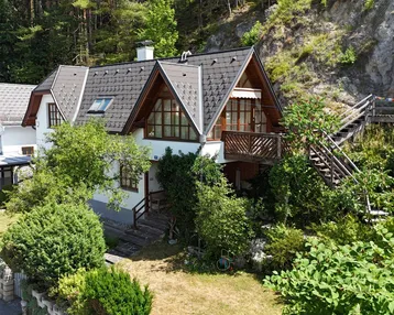 Attraktives Wohnhaus mit Carport und Balkon, umgeben von üppiger Vegetation in ruhiger Umgebung.