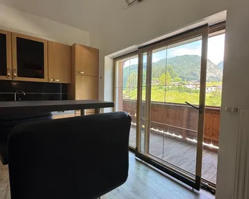Küche mit Barhockern, Holzschränken und beeindruckendem Bergblick durch die Fensterfront.