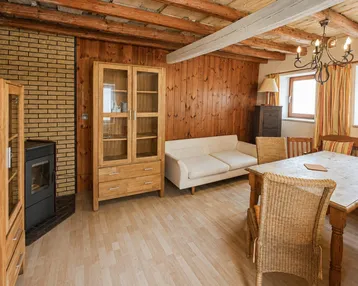 Gemütlicher Wohn-Essbereich mit Holzbalkendecke, Kaminofen und traditionellen Holzmöbeln.