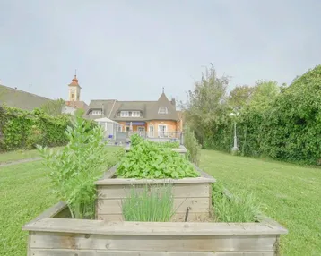 Gepflegter Gartenbereich mit Hochbeeten für den Anbau von Kräutern und Gemüse, im Hintergrund das Wohnhaus.