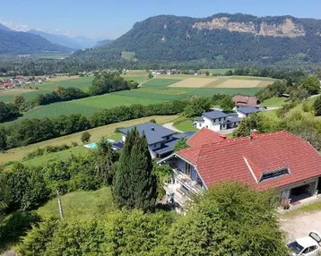 Panoramablick auf ein Haus mit rotem Ziegeldach, umgeben von Natur und Bergen.