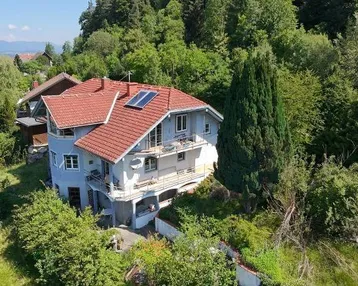 Luftaufnahme eines Hauses mit rotem Ziegeldach, Balkonen und Photovoltaikanlage.