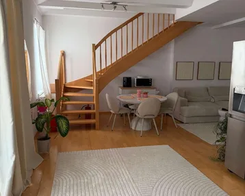Heller offener Wohn- und Essbereich mit Holztreppe, Parkettboden und sichtbaren Deckenbalken.