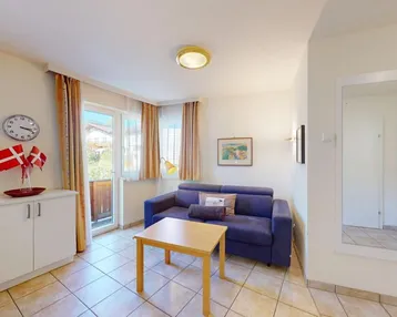 Gemütlicher Wohnbereich mit blauer Couch und Spiegel, bietet Zugang zum sonnigen Balkon.