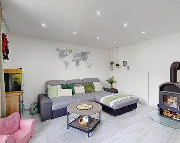 Gemütliches Wohnzimmer mit modernem Sofa, Holzboden und einem stilvollen Kaminofen.