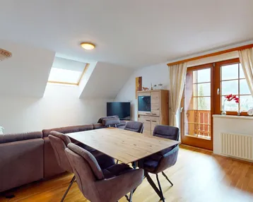 Heller Wohn- und Essbereich mit Holzboden, Dachschräge und Zugang zum Balkon.