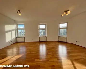Helles, leeres Wohnzimmer mit Parkettboden und mehreren Fenstern, die viel Tageslicht hereinlassen.
