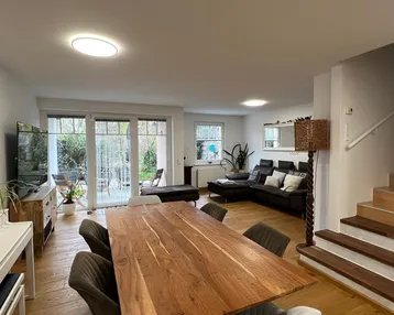 Geräumiger offener Wohn-Essbereich mit Holzboden, großem Esstisch und Zugang zum Garten.