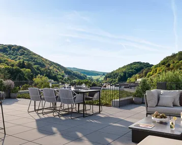 Geräumige Terrasse mit Essbereich und Lounge-Möbeln, umgeben von grünen Hügeln und Weitblick.