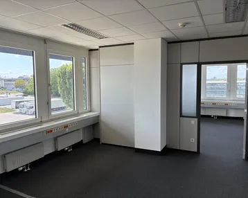 Geräumiges, leeres Büro mit großen Fenstern, modularen Wänden und Blick auf ein Industriegebiet.