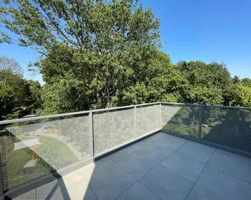 Geräumiger Balkon mit modernem Metallgeländer und Blick ins Grüne unter blauem Himmel.