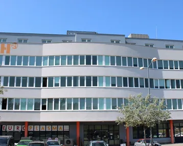Modernes Bürogebäude mit geschwungener Fassade und vielen Fenstern unter blauem Himmel.