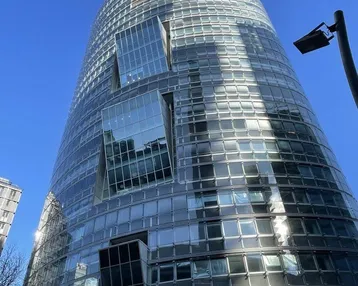 Beeindruckendes modernes Hochhaus mit gläserner Fassade und markanter Architektur unter blauem Himmel.