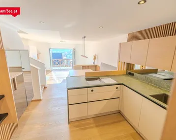 Moderne Küche mit hellen Holzfronten, grüner Arbeitsplatte und Zugang zu einem Balkon mit Bergblick.
