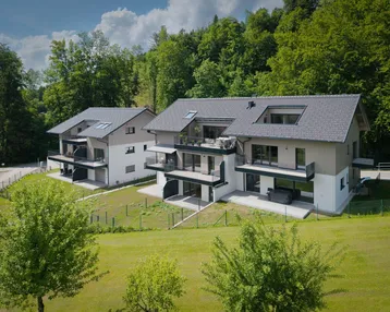 Moderne Mehrfamilienhäuser mit Balkonen und Terrassen, eingebettet in eine grüne Hügellandschaft.