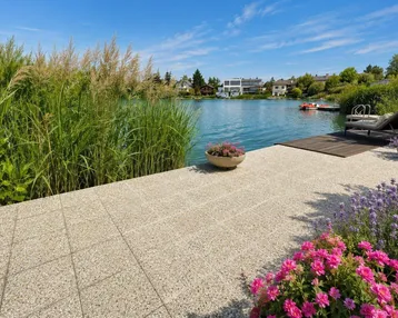 Gepflasterte Terrasse am Seeufer mit Schilf, Blumen und Liegestühlen, ideal zum Entspannen.